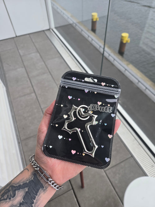 Hand holding a black wallet with a silver carabiner inside and heart patterns, outdoor background